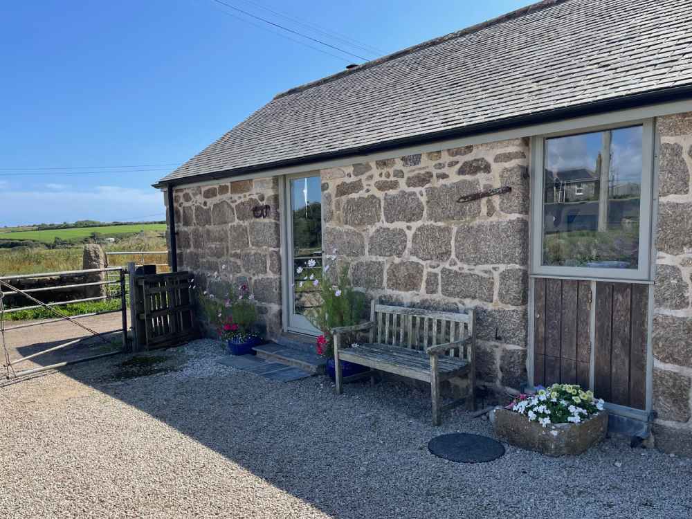 Photo of front door and courtyard of Trengothal Barn with pots of flowers either side of door and a wooden bench